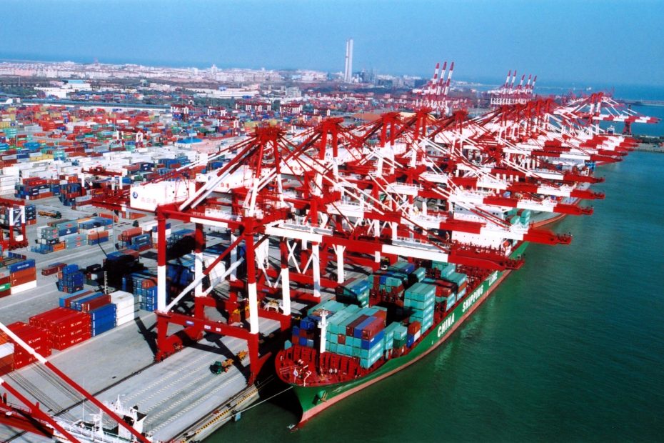 Busy port with cranes and container ships docked, illustrating high activity in the global shipping industry GEOTRENDS.EU
