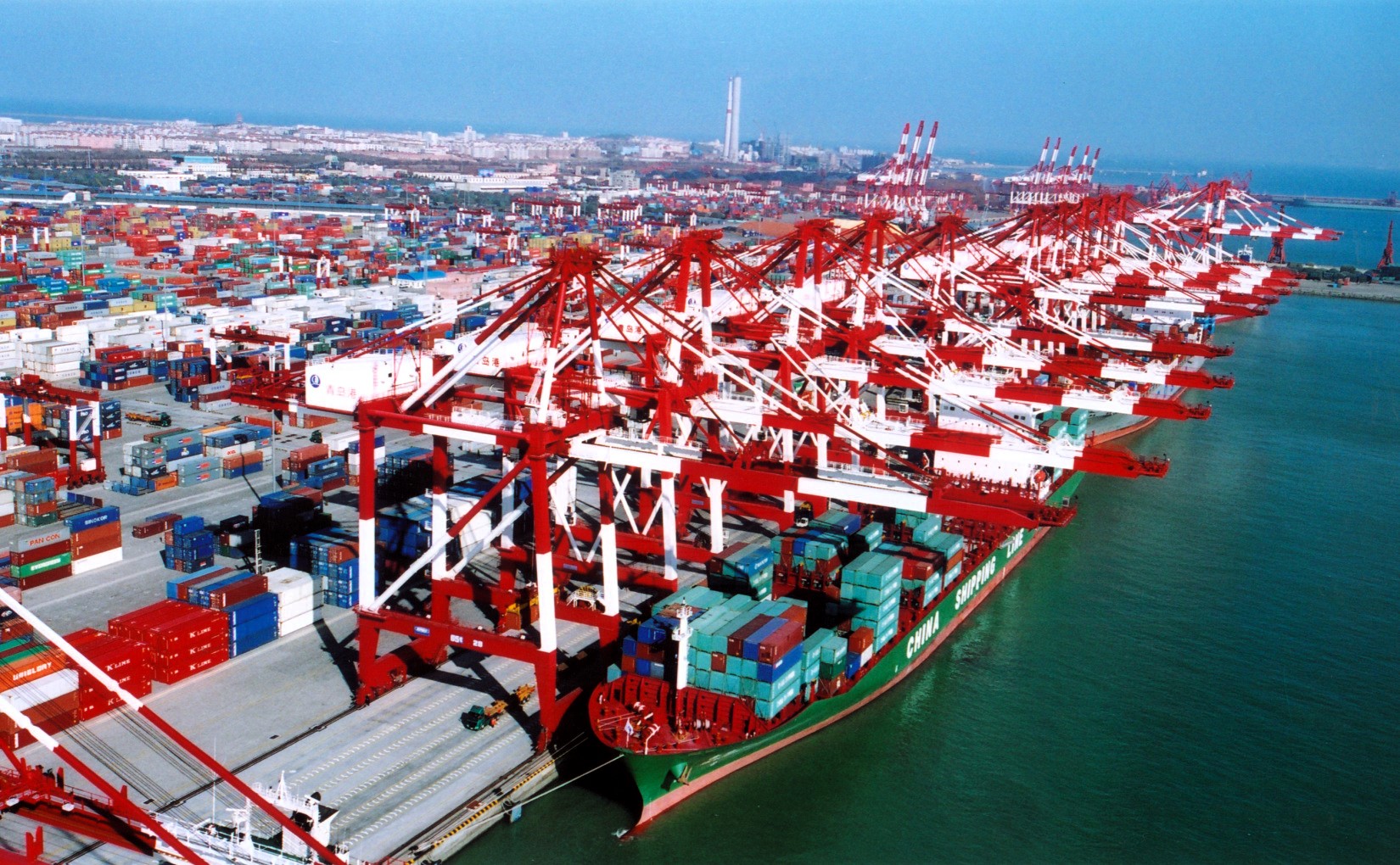Busy port with cranes and container ships docked, illustrating high activity in the global shipping industry GEOTRENDS.EU