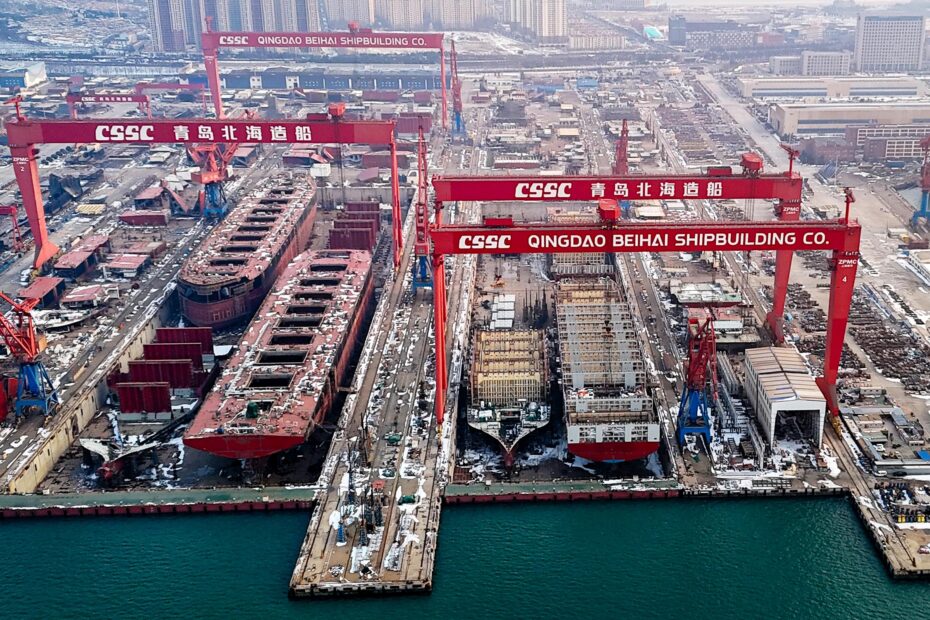 Aerial view of a massive Chinese shipyard, showcasing multiple large ships under construction. Towering red gantry cranes labeled “CSSC Qingdao Beihai Shipbuilding Co.” dominate the scene, emphasizing China’s industrial scale. The shipyard is filled with steel structures, construction equipment, and docks extending into the water, illustrating the sheer capacity of China’s maritime manufacturing sector