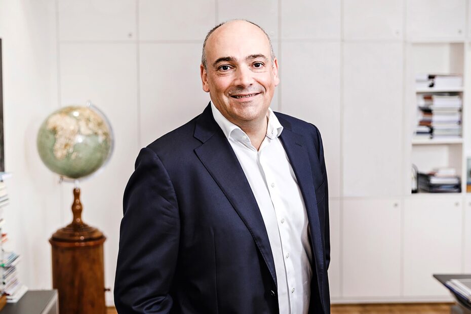 Rolf Habben Jansen, CEO of Hapag-Lloyd, smiling in his office with a globe and books in the background