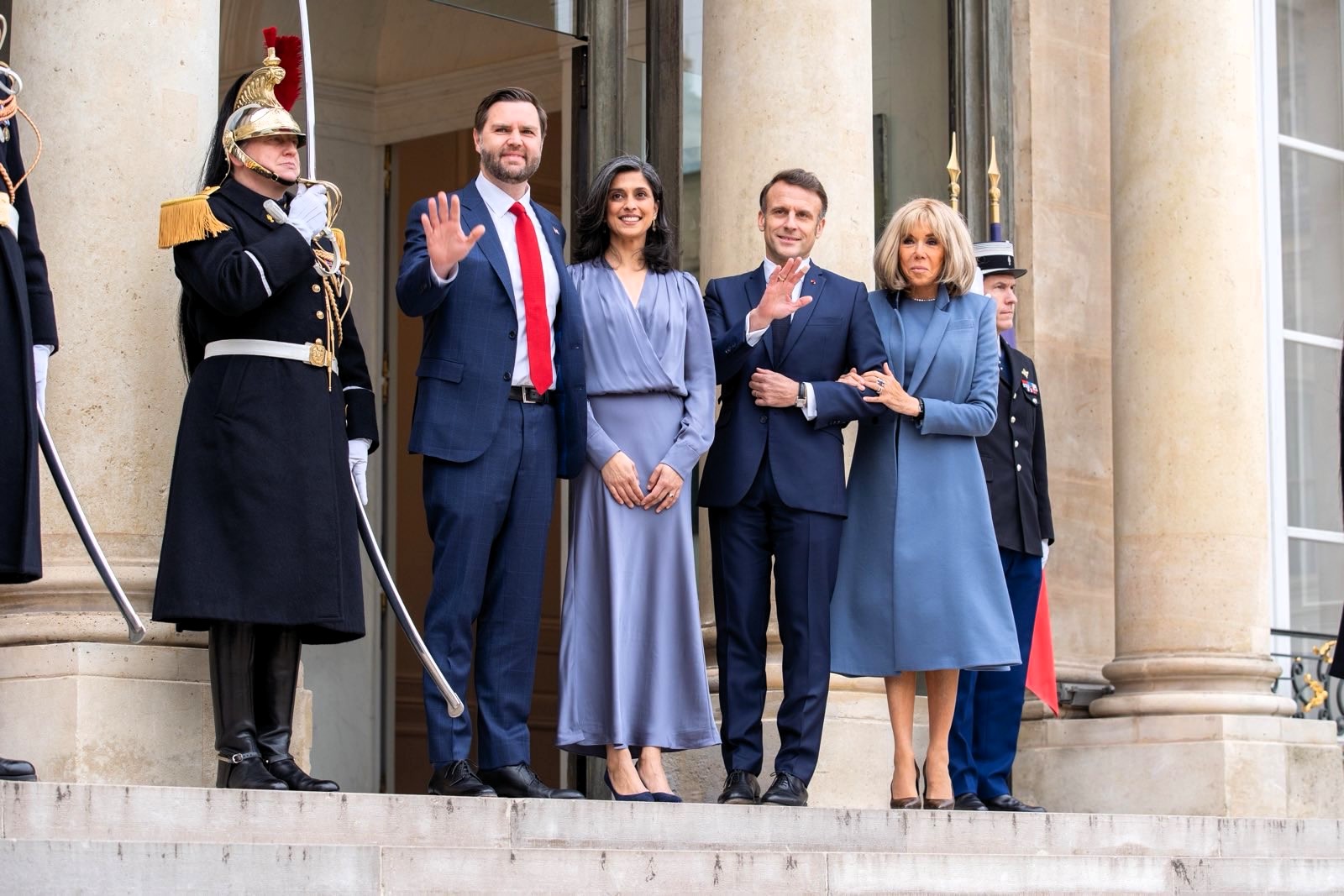 JD Vance and his wife stand with Emmanuel and Brigitte Macron on the steps of the Élysée Palace, waving to the press, as ceremonial guards stand at attention