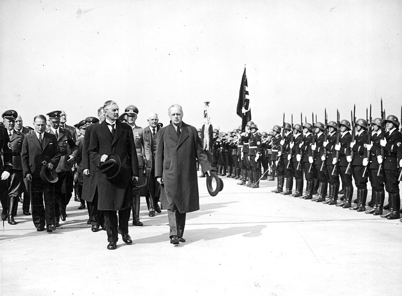 Neville Chamberlain, accompanied by officials, walks past a German military honor guard upon his arrival at Munich airfield on September 29, 1938