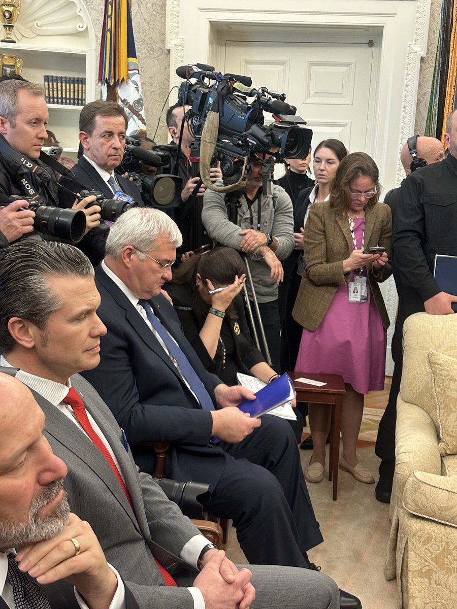 A crowded Oval Office scene with journalists, diplomats, and officials. Oksana Markarova, Ukraine’s ambassador to the U.S., sits with her head in her hand, visibly distressed. Cameras and reporters focus on the ongoing meeting, while attendees display mixed emotions