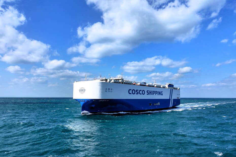 he Wen Jing Kou, a large COSCO Shipping dual-fuel vehicle carrier, sails across the open sea under a bright blue sky with scattered clouds