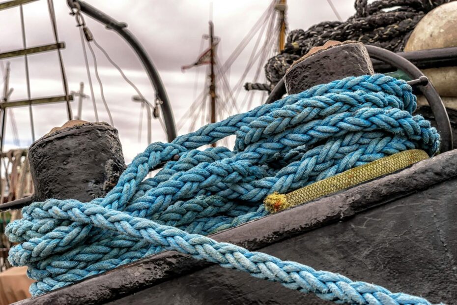 Close-up of thick blue mooring ropes coiled on a weathered black bollard aboard a docked commercial vessel