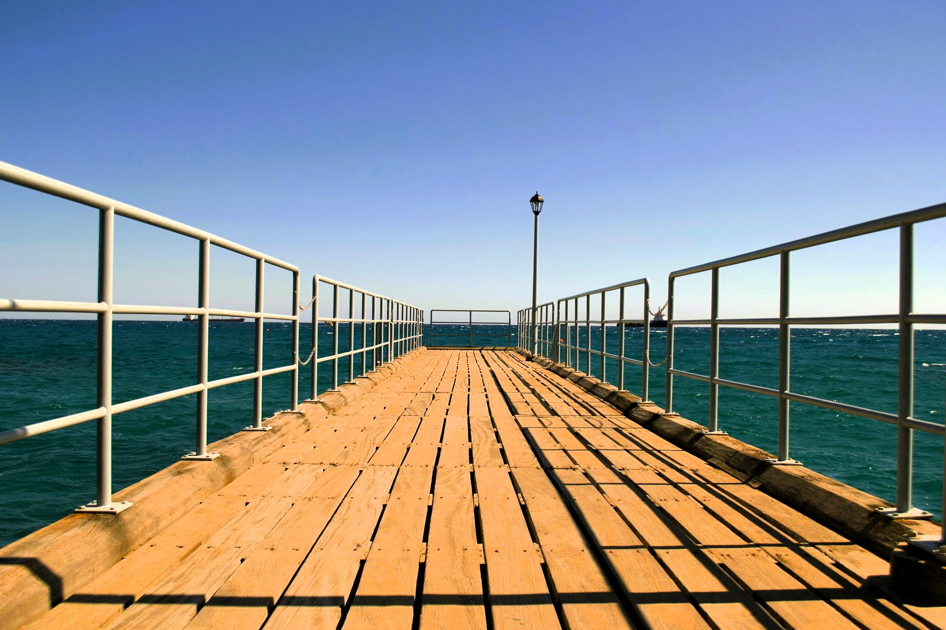Wooden pier extending into the sea under clear blue sky, symbolizing resilience and ongoing maritime journeys