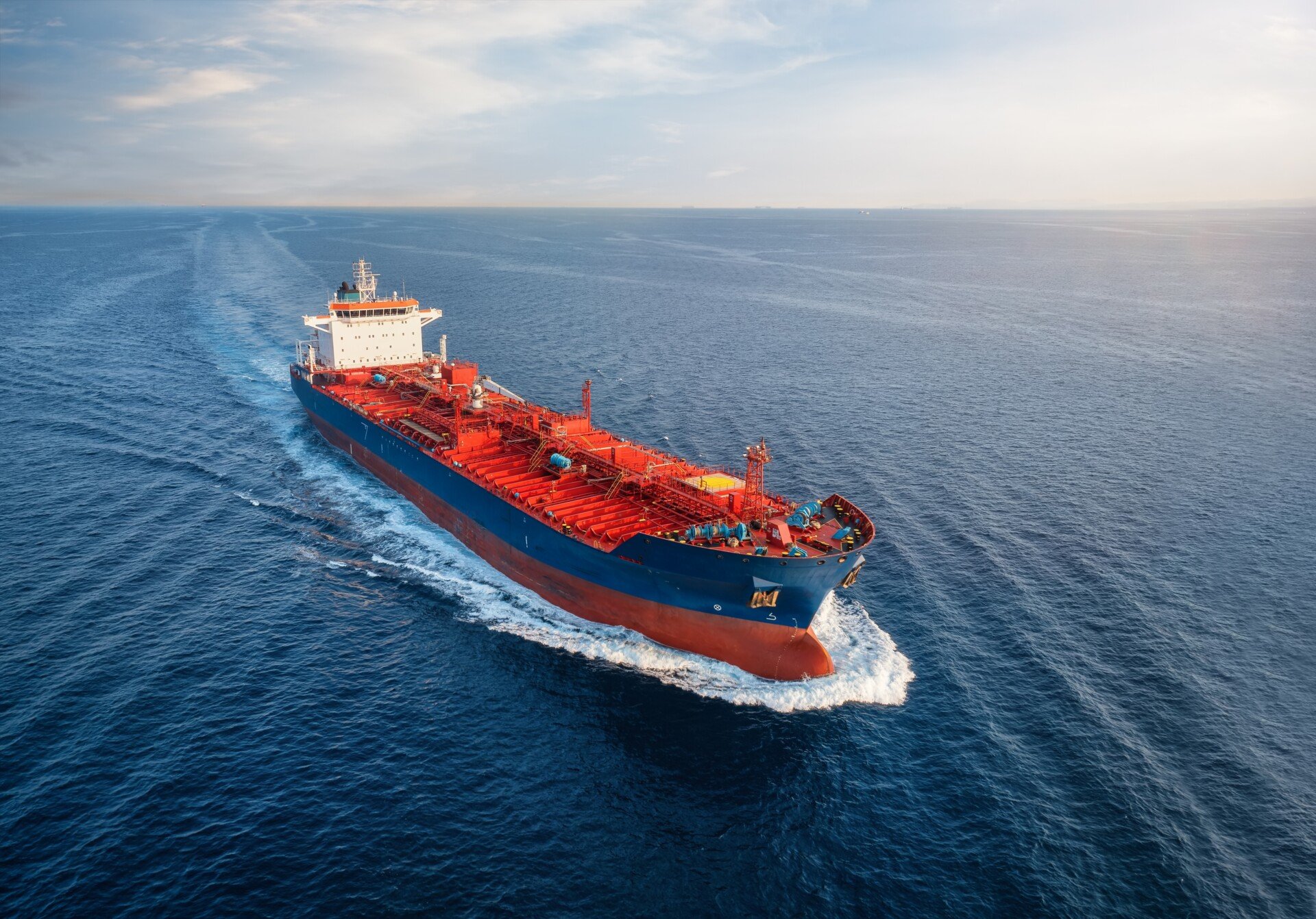 Large cargo vessel sailing at sea under clear sky, photographed from above, showing deck structures and open ocean surroundings