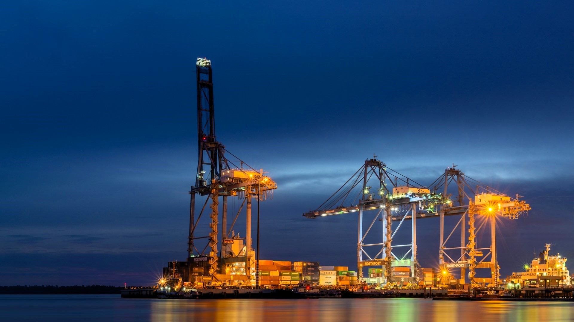 Night view of Port Klang in Tanjung Harapan with illuminated container cranes, stacked cargo containers, and vessel
