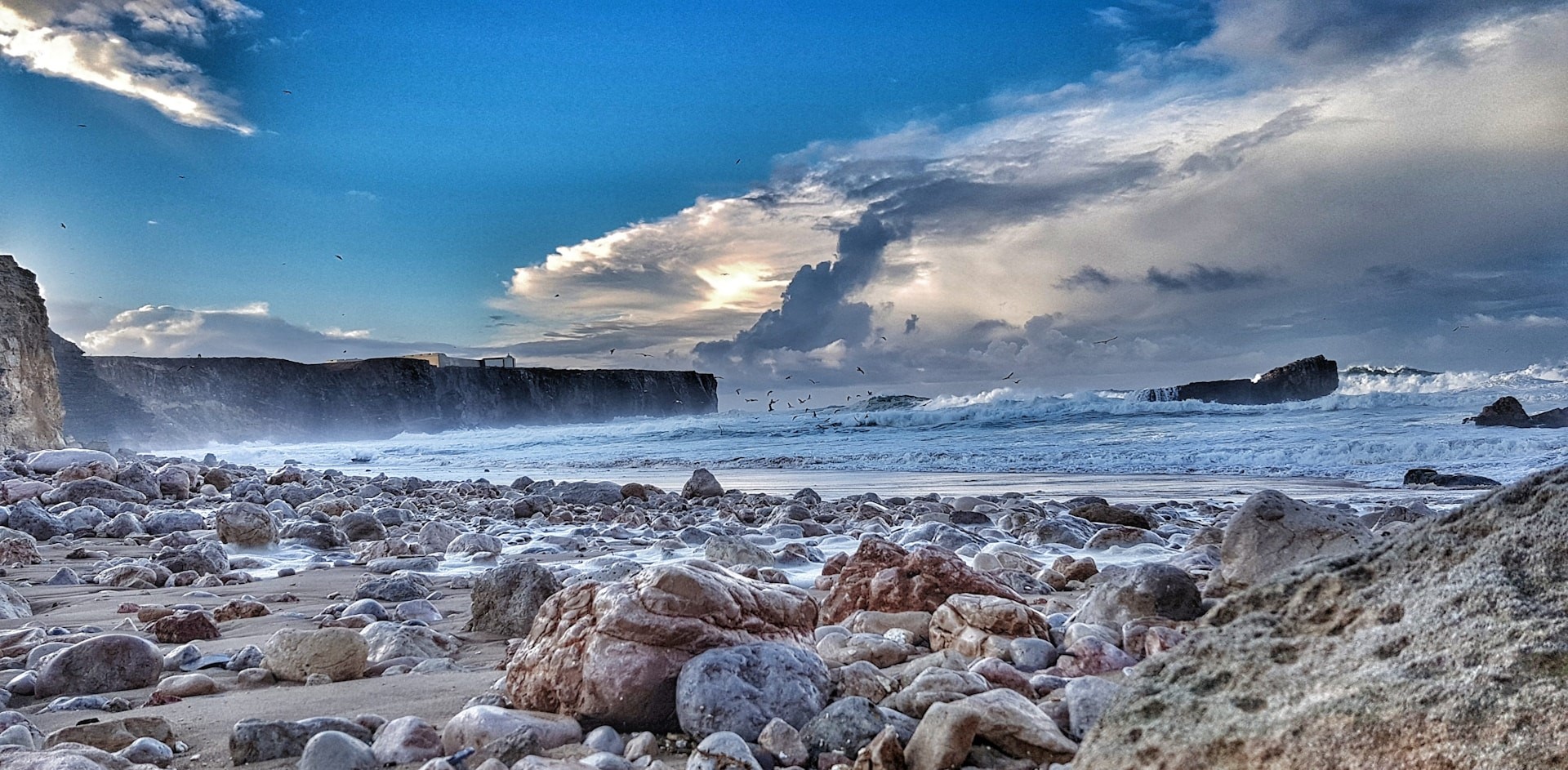 Dramatic seascape with turbulent waves crashing against rocky coastline under stormy skies with seabirds flying overhead