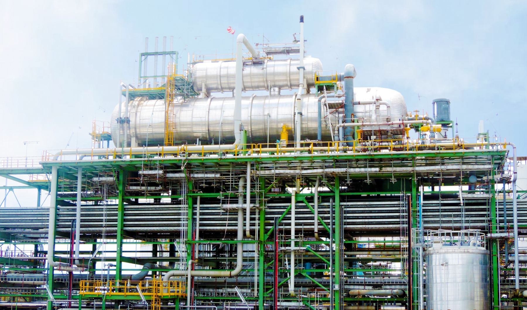 Close-up of the Dangote Petroleum Refinery and Petrochemicals complex in Nigeria, showing large silver processing vessels and green industrial piping against a bright sky
