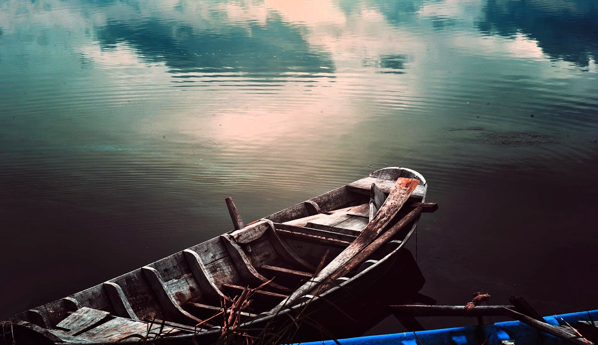 Weathered wooden rowboat resting on calm reflective water at dusk, soft ripples and muted sky mirrored on the surface