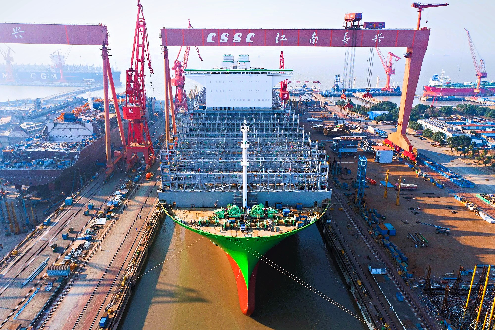Aerial view of a large container ship under construction at CSSC Jiangnan Changxing Shipyard in Shanghai, China, surrounded by towering red gantry cranes
