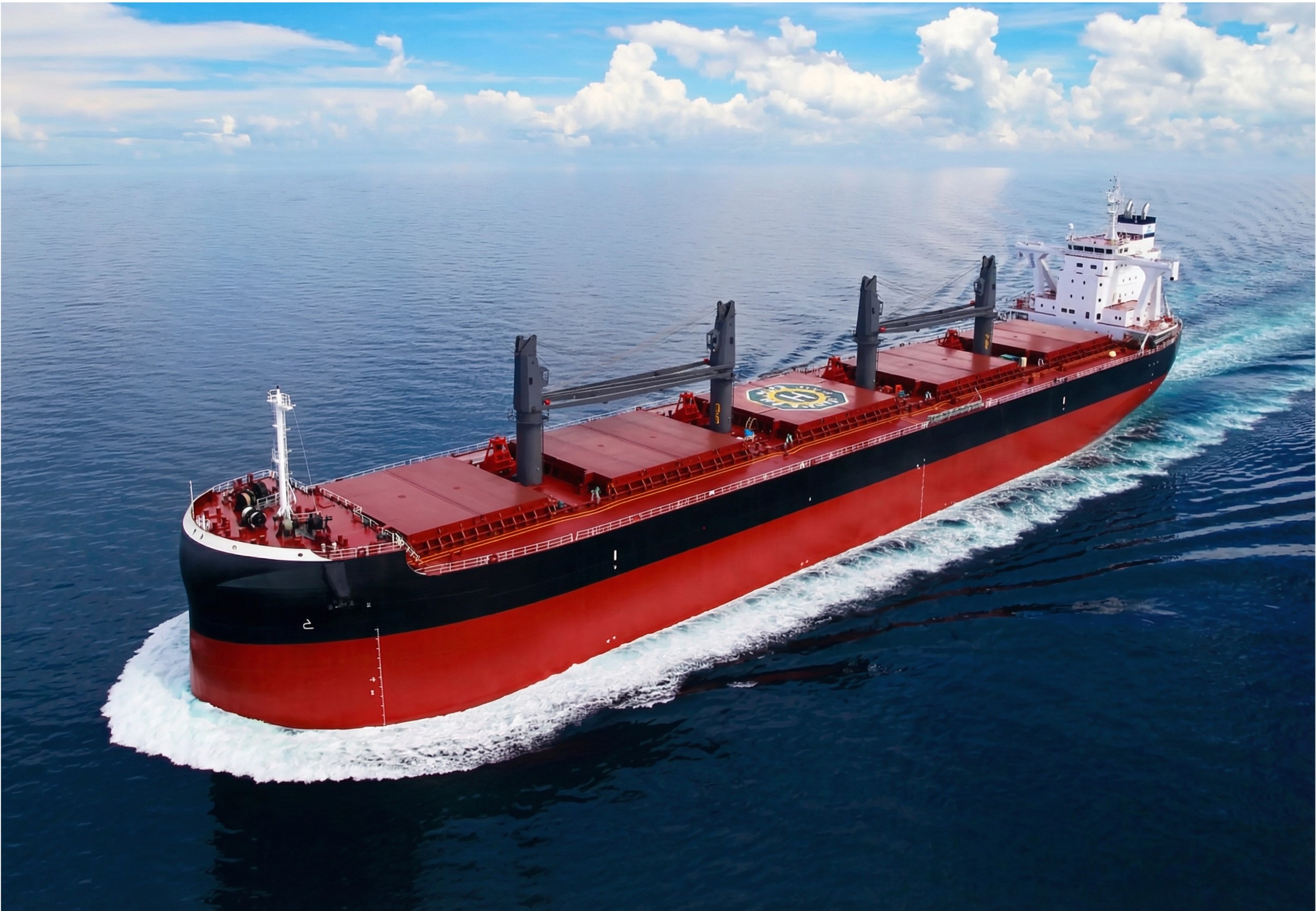 Red and black Ultramax bulk carrier sailing across open ocean under blue sky with scattered clouds, viewed from aerial perspective