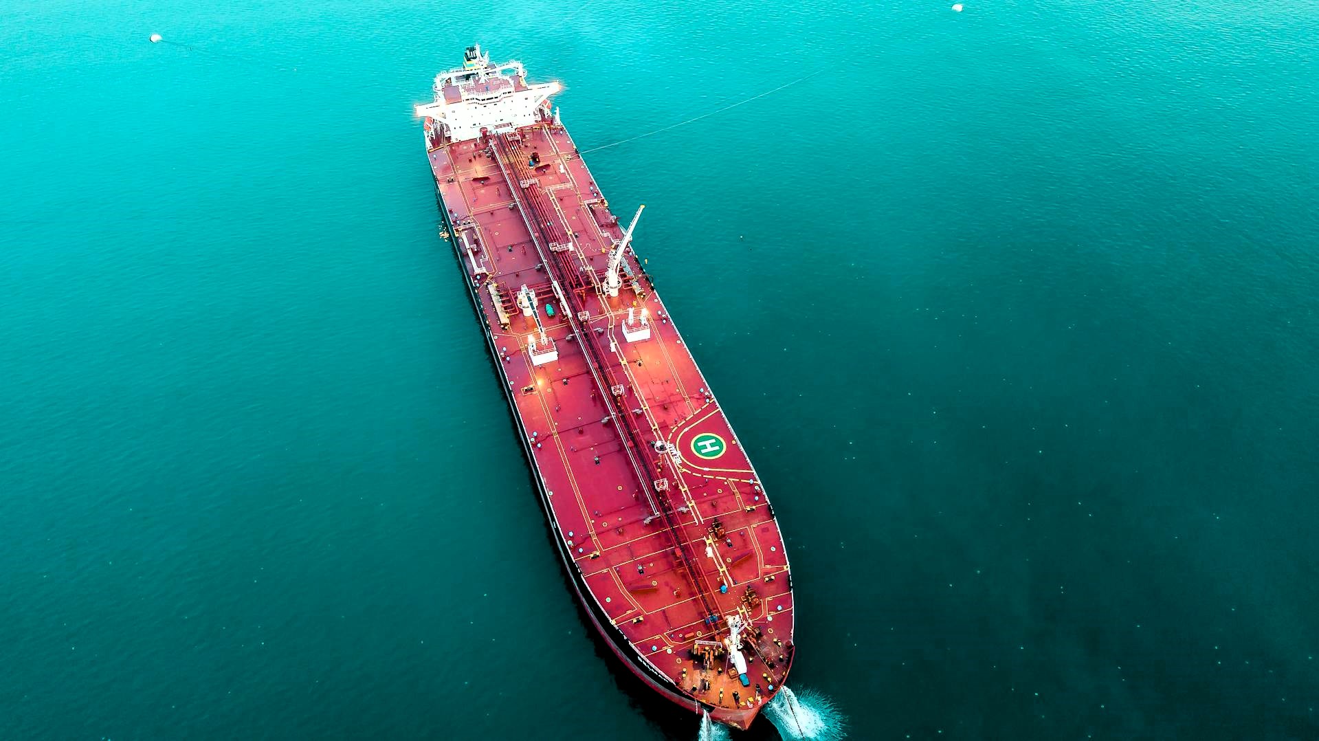 Aerial view of a crude oil tanker underway on open turquoise water, helipad visible amidships