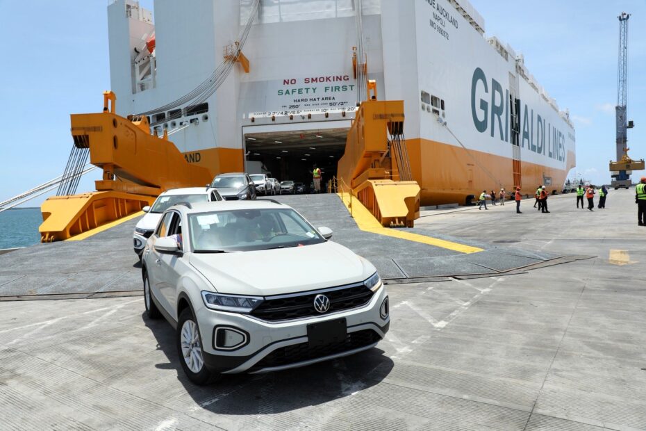 White Volkswagen T-Roc SUVs drive down the loading ramp of the Grande Auckland car carrier, operated by Grimaldi Lines, at the Port of Lamu in Kenya, with port workers in high-visibility vests directing the offloading operation