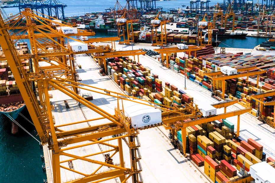 Container terminal with cranes and stacked shipping containers at the Port of Piraeus, overlooking the sea and surrounding hills