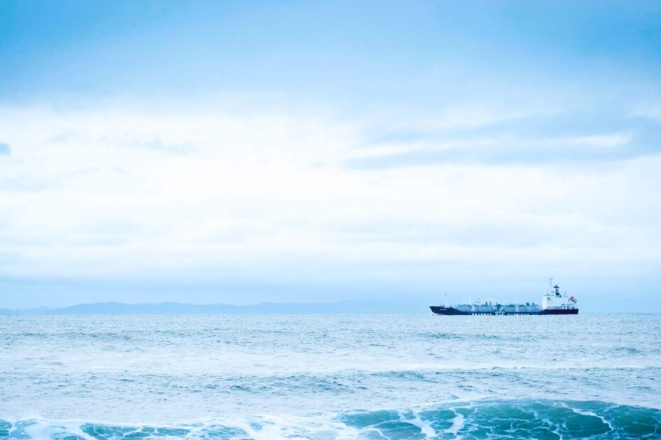 Distant oil tanker on open sea under muted sky, minimal composition with wide horizon and subdued tones