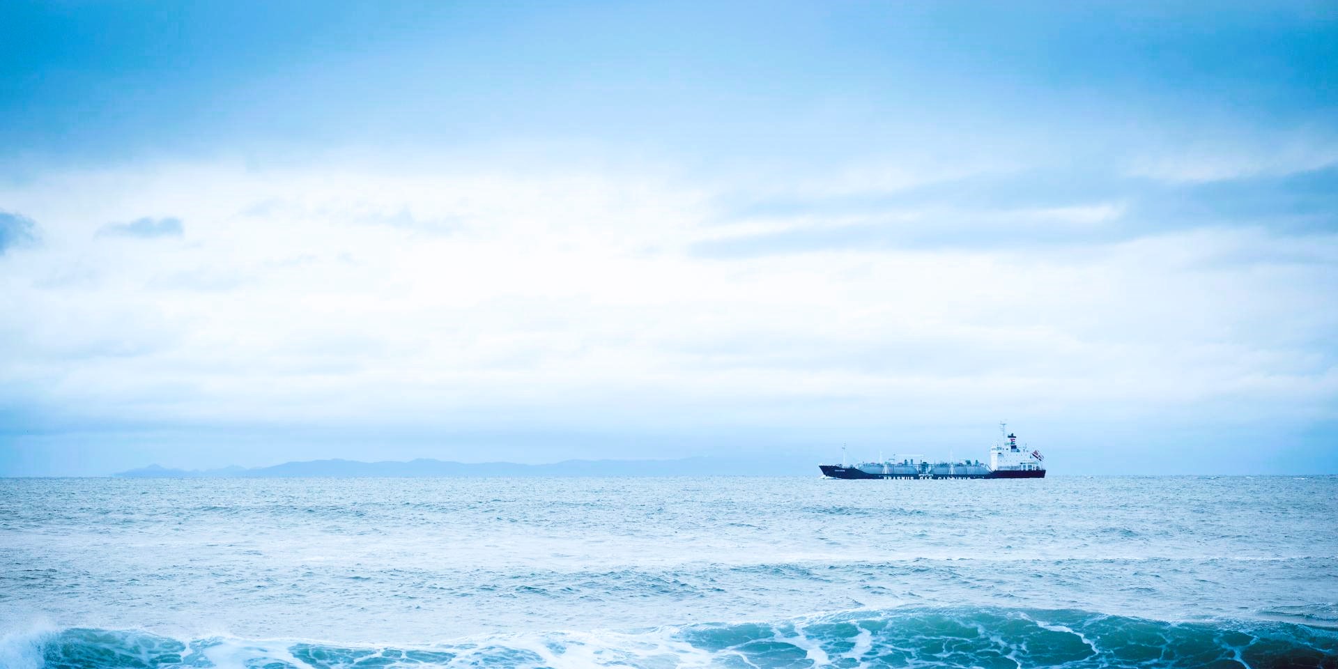 Distant oil tanker on open sea under muted sky, minimal composition with wide horizon and subdued tones