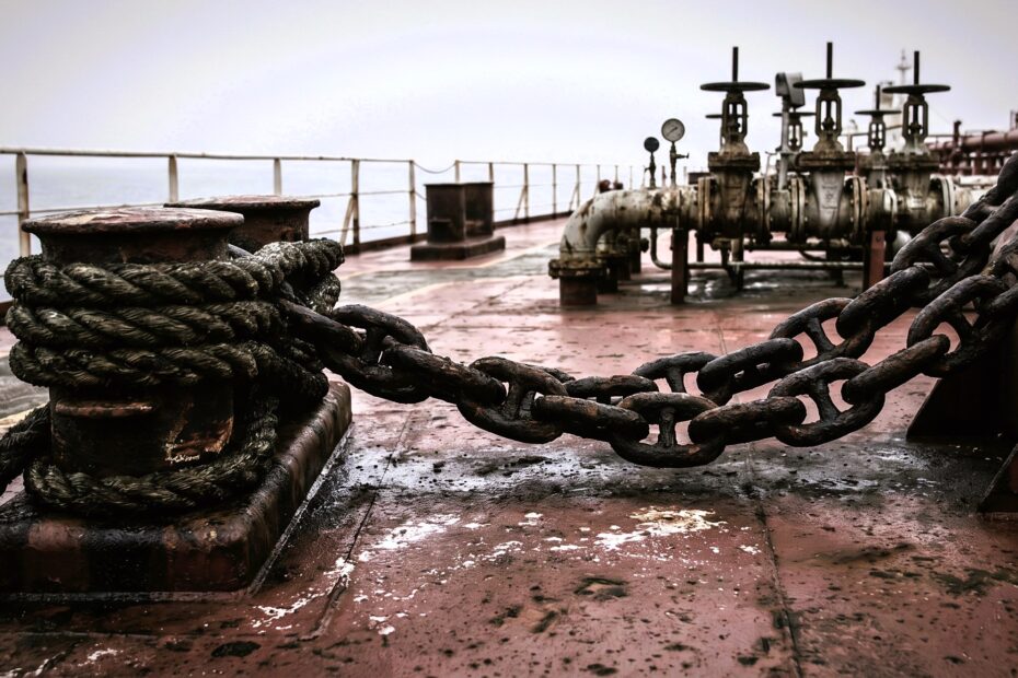 Close-up of heavy chain and mooring lines on an oil tanker deck under grey sky, suggesting tension and immobility at sea