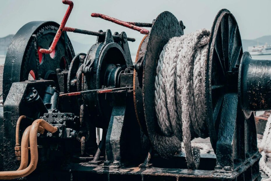 Close-up of a ship’s winch with steel cable and rope, showing worn metal, rust, and industrial maritime equipment on deck