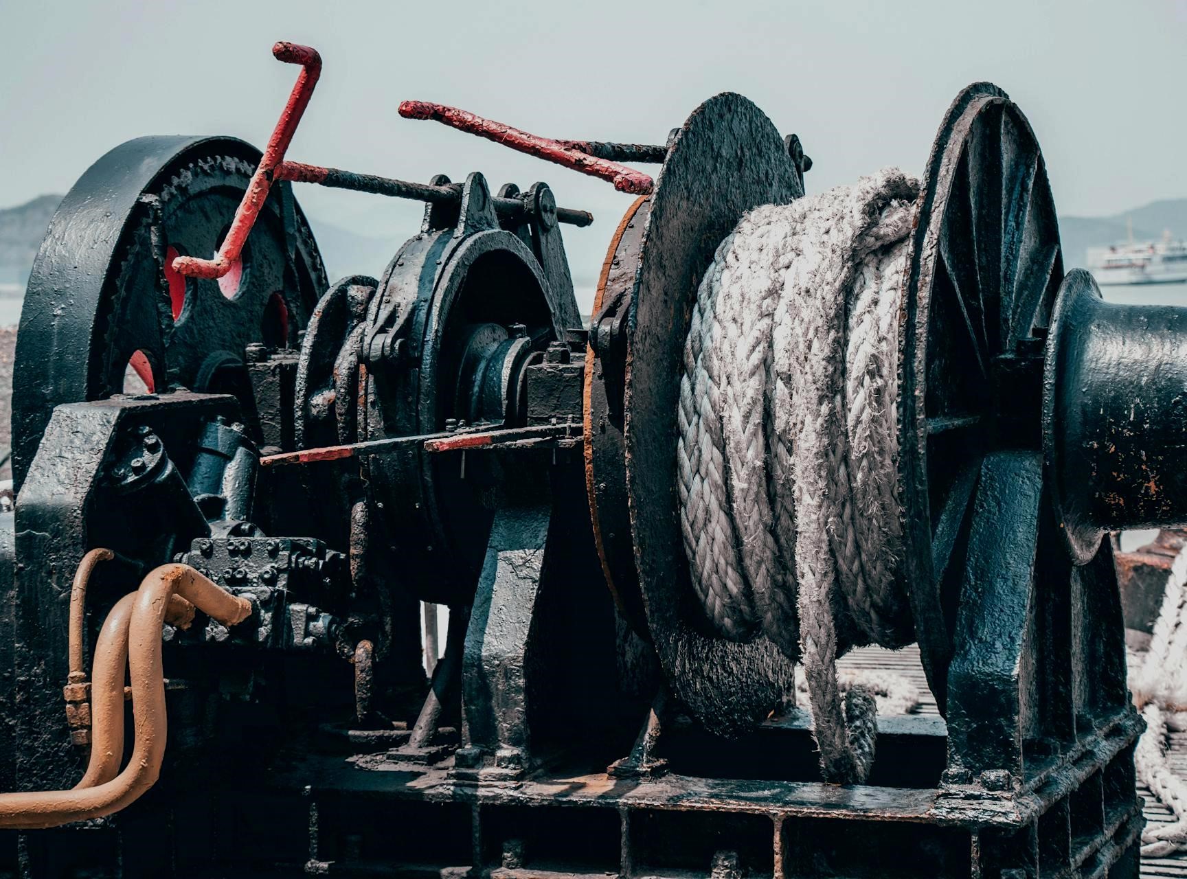 Close-up of a ship’s winch with steel cable and rope, showing worn metal, rust, and industrial maritime equipment on deck