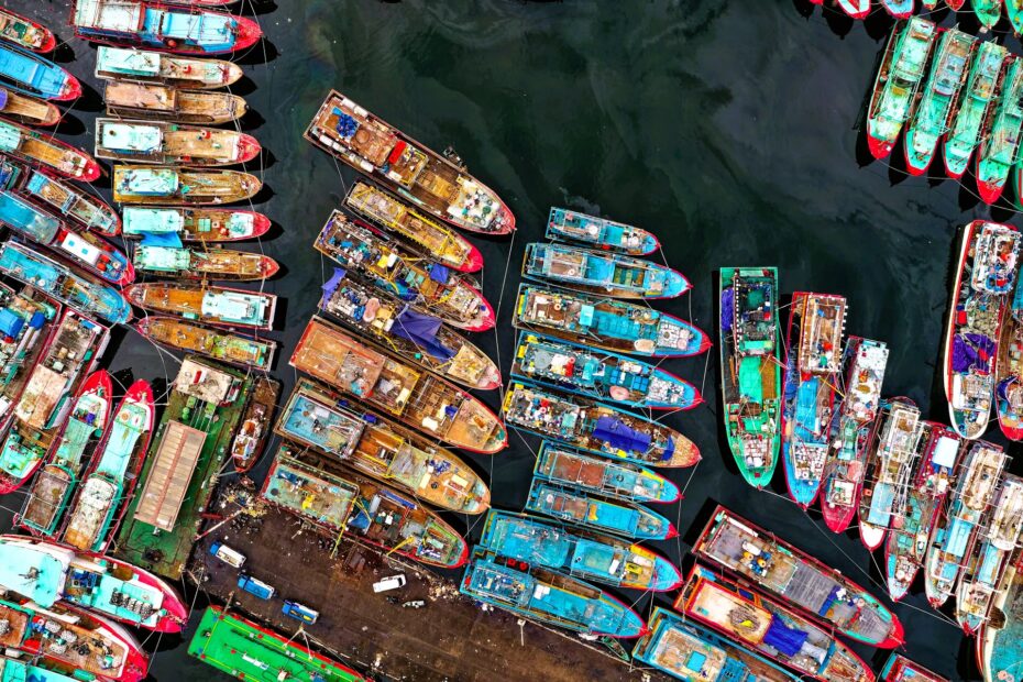 Aerial view of tightly packed colorful vessels moored in dark harbour waters, forming dense geometric patterns across a busy maritime dock