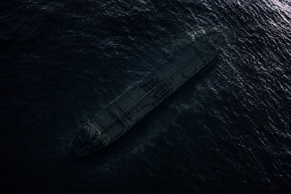 Dark aerial view of a shadowy VLCC tanker barely visible beneath black ocean water, creating a minimalist and atmospheric maritime scene
