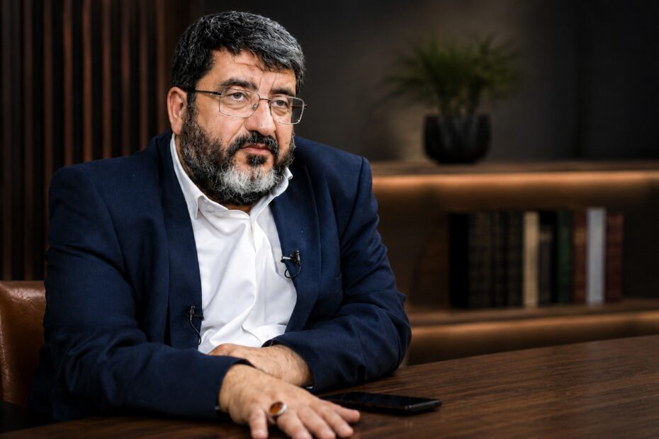 Portrait of Dr. Foad Izadi seated at a desk during an interview, wearing a navy blazer and white shirt in a professional office setting