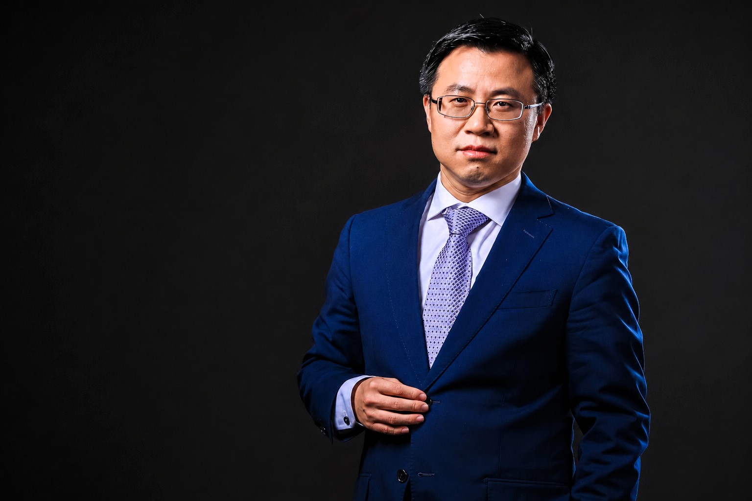 Studio portrait of Professor Wang Dong wearing a dark blue suit and tie against a black background, looking directly at the camera with a composed and professional expression