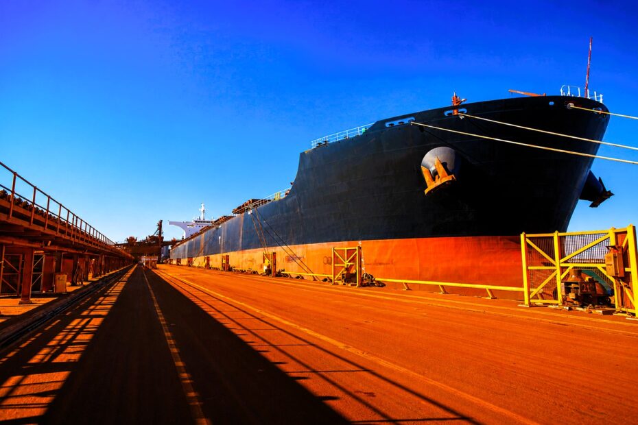 A Capesize bulk carrier berthed at an iron ore export terminal, highlighting the scale of dry bulk logistics, loading infrastructure, and global commodity flows