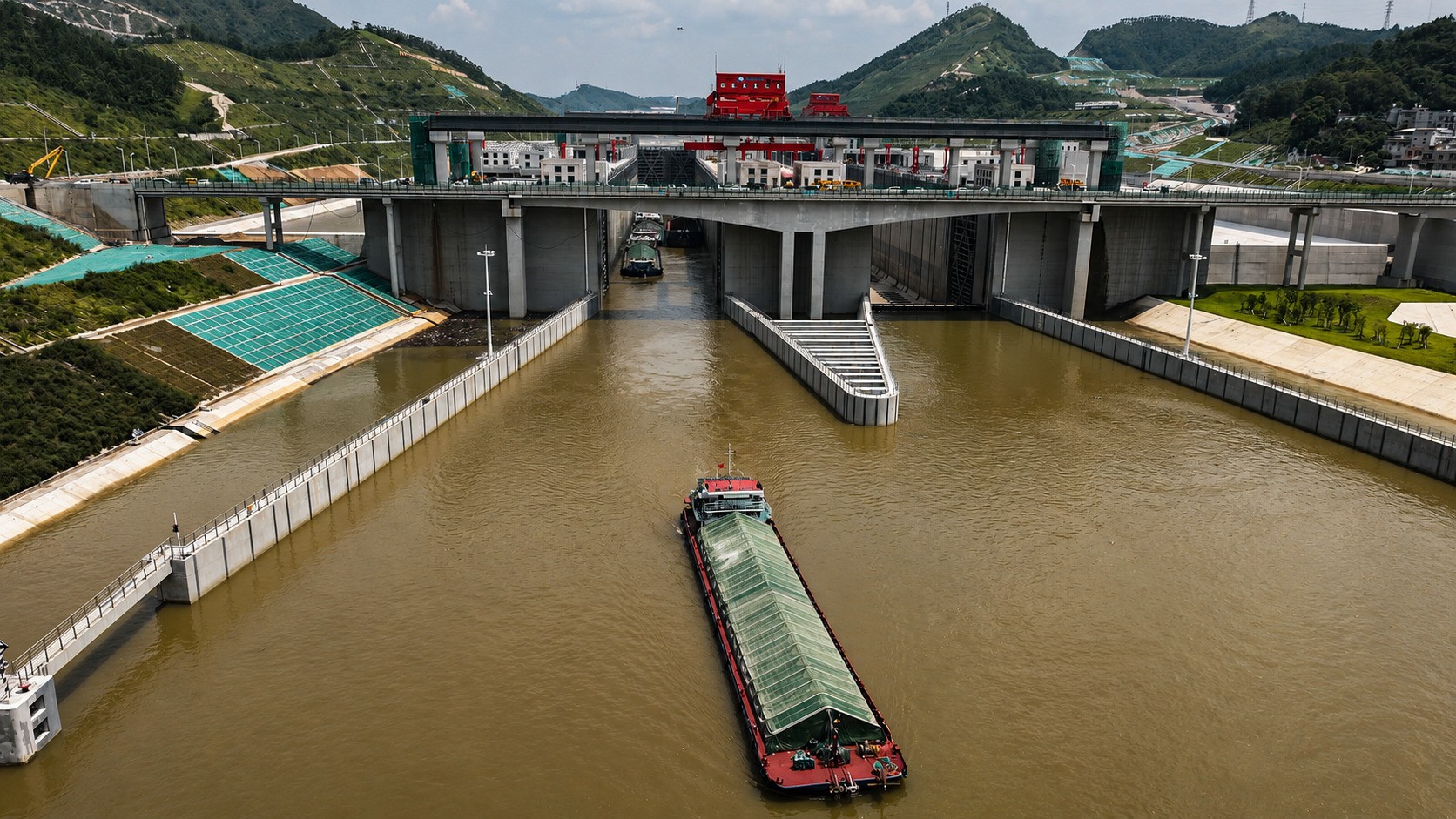 Aerial view of a green-covered cargo barge exiting a concrete lock chamber on the Pinglu Canal near Qinzhou, in Guangxi, southern China