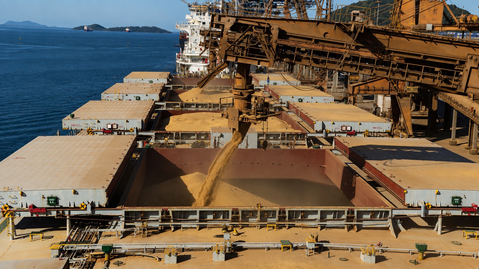 Bulk carrier loading grain at a modern export terminal, with cargo pouring into open holds beneath heavy loading equipment on a clear day