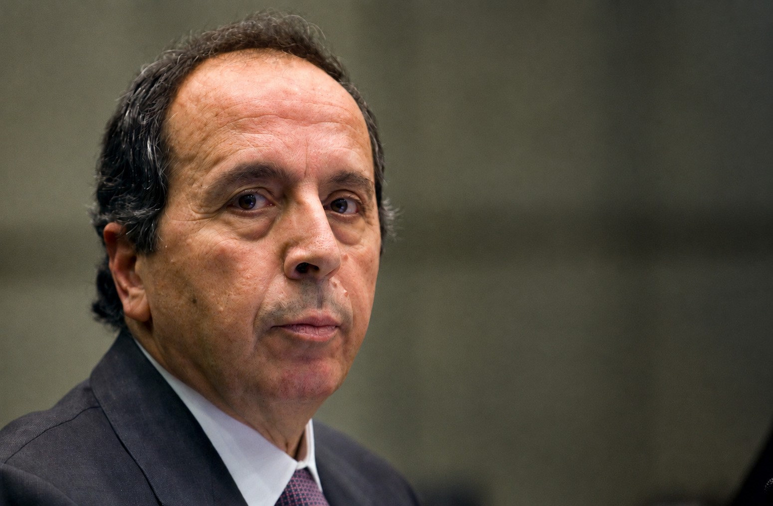 Portrait of General Jamil el-Sayyed in a dark suit against a muted olive-grey background