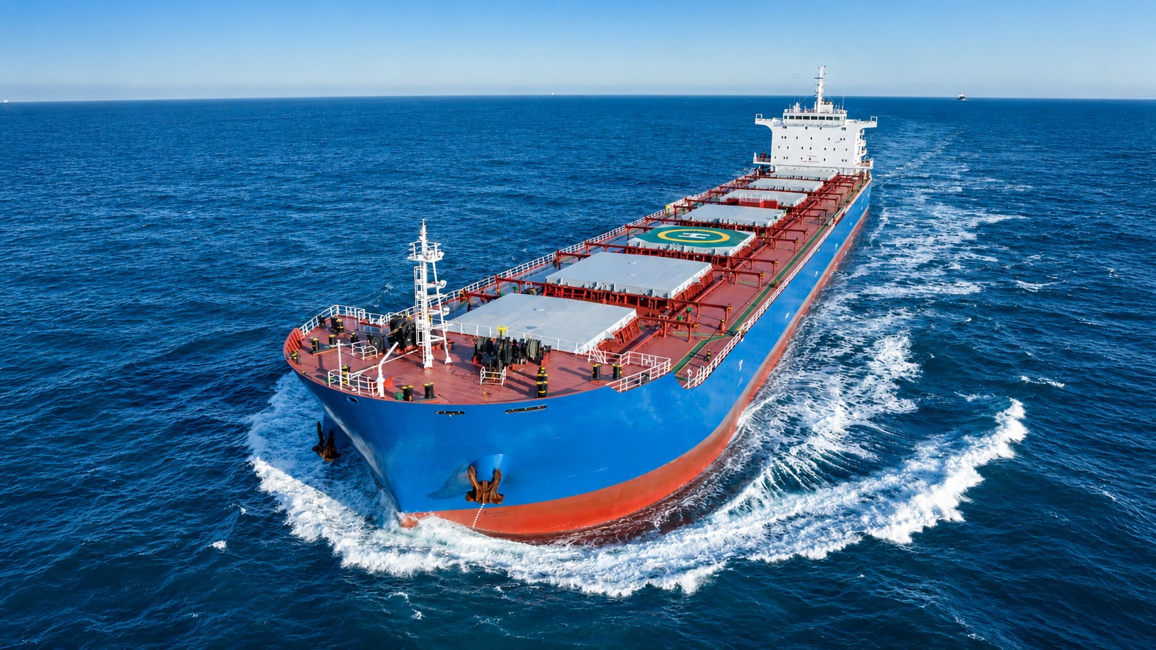 Bulk carrier underway at sea, viewed from an elevated angle as it cuts through open water