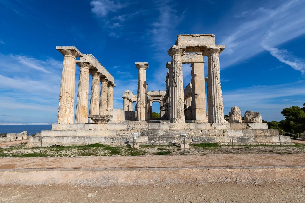 Ancient Doric columns and stone ruins of the Temple of Aphaia on Aegina, overlooking the Saronic Gulf beneath a blue sky