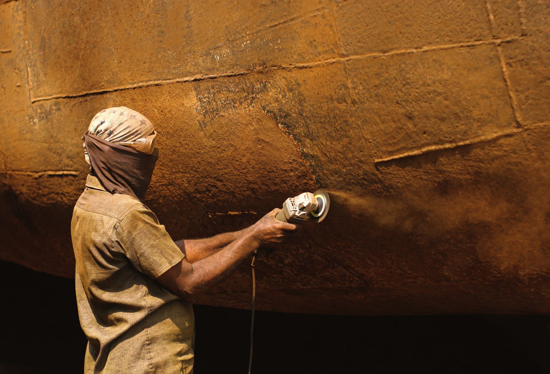 Worker using an angle grinder to remove rust from a ship’s curved steel hull