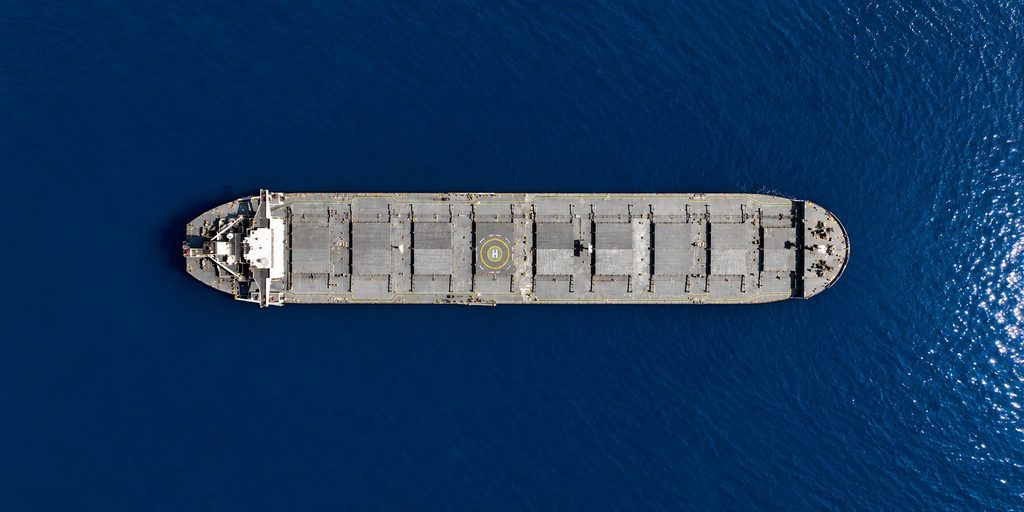 Top-down aerial view of a grey bulk carrier surrounded by vast, deep-blue waters, illustrating the importance of vessel positioning and strategic decisions in the Ultramax and Handysize freight markets